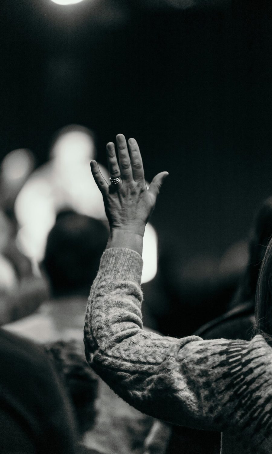 Black and white photo of a woman raising her hand in an audience, capturing engagement and curiosity.